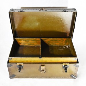 May include: An antique metal trunk with a brass latch and hinges. The trunk is open and has a wooden interior with two compartments.