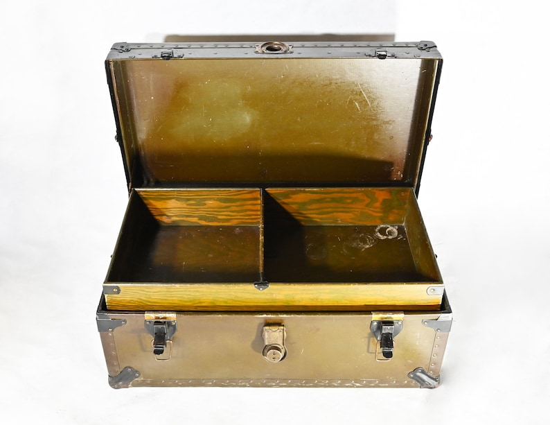 May include: An antique metal trunk with a brass latch and hinges. The trunk is open and has a wooden interior with two compartments.