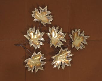 May include: A wall decoration featuring six gold metal maple leaves connected by thin black metal stems. The leaves are arranged in a cluster, with some overlapping.