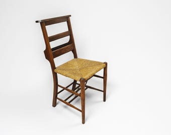 Silla antigua de madera maciza con asiento tejido de junco y estante de almacenamiento.