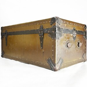 May include: A vintage, rectangular, brown metal trunk with black metal accents and hardware. The trunk has a distressed look and is secured with metal clasps.