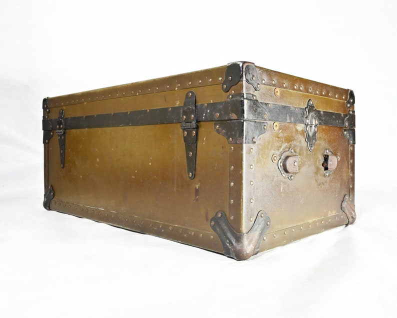 May include: A vintage, rectangular, brown metal trunk with black metal accents and hardware. The trunk has a distressed look and is secured with metal clasps.