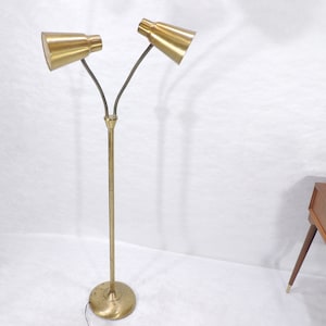 May include: A gold floor lamp with two adjustable arms and shades. The lamp has a simple, mid-century modern design.
