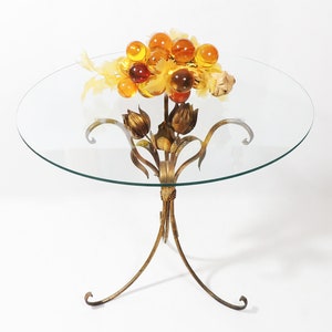 May include: A glass-top table with a gold metal base in the shape of stylized flowers. The table top has a cluster of amber glass grapes on it.