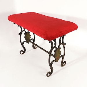 May include: A red velvet bench with decorative dark metal legs. The legs have leaf accents and scrolled feet. The bench is rectangular and sits on a white background. The bench measures approximately 100 cm in length.