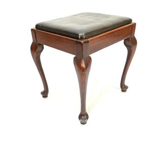 May include: A dark brown wooden stool with a black leather seat and cabriole legs.