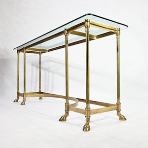Op de afbeelding: Een messing consoletafel met een glazen blad en gebogen poten. De tafel heeft een eenvoudig, elegant ontwerp en zou een geweldige aanvulling zijn op elk huis.