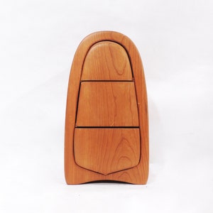 Pu&ograve; includere: Una scatola di legno con una forma curva a forma di lacrima e tre cassetti. La scatola &egrave; realizzata in legno marrone chiaro con una finitura naturale.