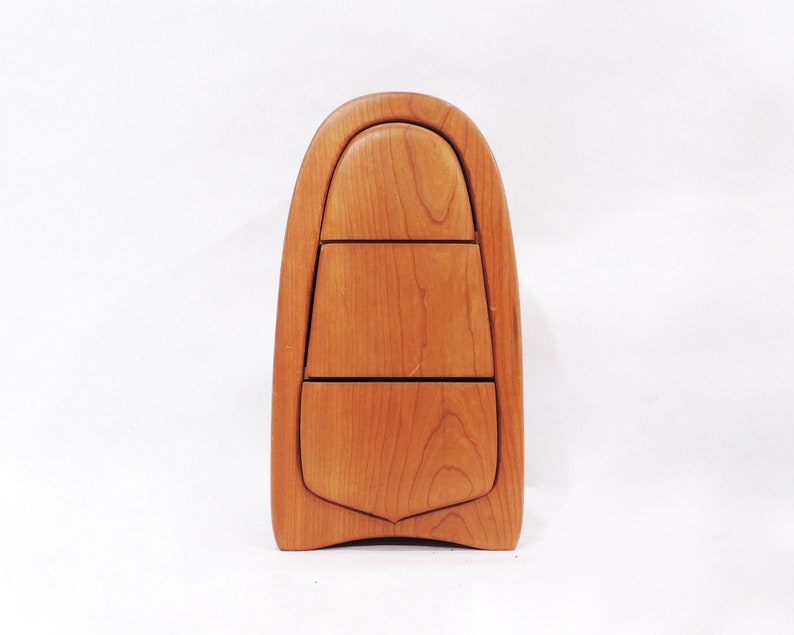 Pu&ograve; includere: Una scatola di legno con una forma curva a forma di lacrima e tre cassetti. La scatola &egrave; realizzata in legno marrone chiaro con una finitura naturale.