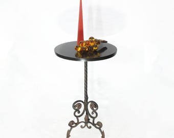 Soporte de mesa redondo para plantas con tablero de piedra negra y pátina envejecida sobre metal.