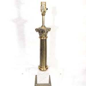 Peut inclure: Une lampe en laiton avec un design de colonne cannelée, surmontée d'un chapiteau orné et d'un luminaire. La lampe repose sur une base en marbre blanc, avec un élément décoratif en laiton en dessous. Un élément de décoration intérieure classique et élégant.