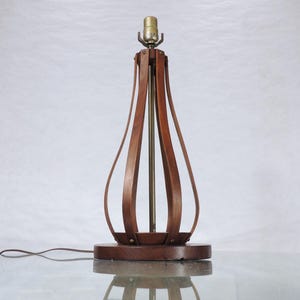 May include: A wooden table lamp with a curved, geometric design. The lamp has a brass base and a brown wooden shade.