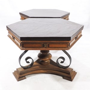 May include: Two hexagonal wooden tables with black slate tops and ornate iron scrollwork bases. The tables are nested together.
