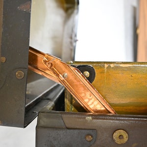 May include: A vintage metal suitcase with a copper hinge. The suitcase is open and the inside is lined with wood.