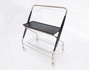 May include: A chrome and black folding bar cart with a black top shelf and a chrome wire bottom shelf. The cart has four wheels and is in a folded position.