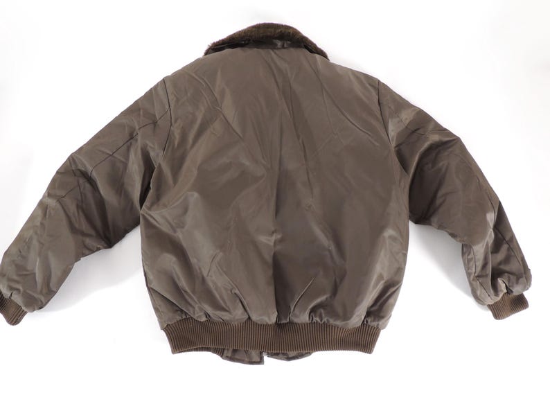 May include: A brown bomber jacket with a faux fur collar. The jacket has a ribbed hem and cuffs, and a quilted design on the back. The jacket is made of a smooth, shiny material.