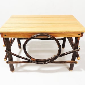 Op de afbeelding: Een rustieke houten salontafel met een naturel houten blad en een unieke, gedraaide takkenbasis. De tafel heeft een ronde opening in de basis, wat bijdraagt aan het unieke ontwerp.