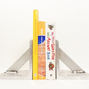 May include: A pair of silver metal bookends holding up three books. The book on the left is yellow and says "World History Encyclopedia". The middle book is orange and says "Wow! Utah Canyon Country". The book on the right is colourful and says "My First Question and Answer Book".