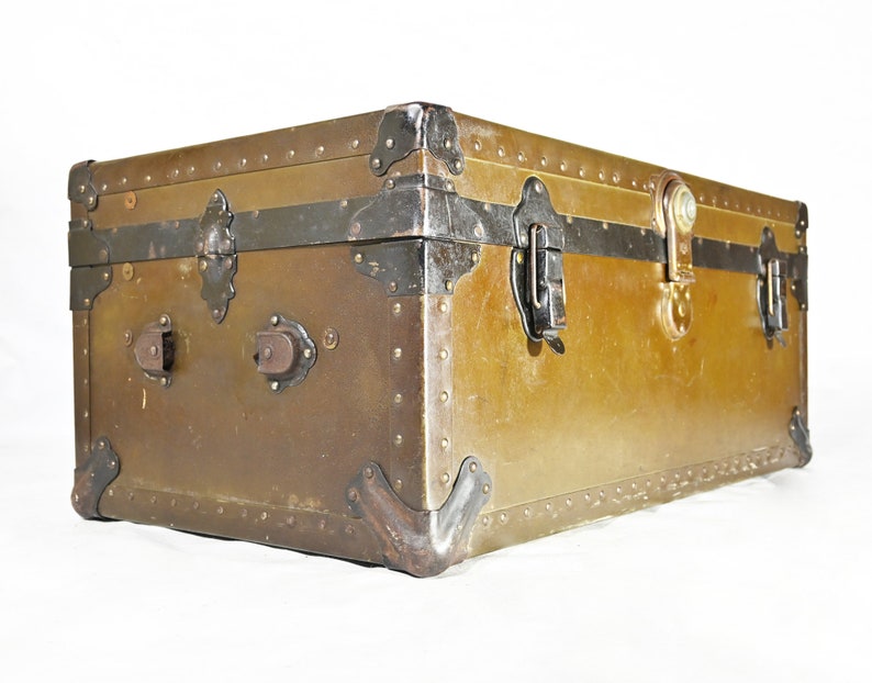 May include: A vintage metal trunk with a green patina finish and black metal hardware. The trunk has a hinged lid with two clasps and a lock. The trunk is decorated with rivets and has a worn, distressed look.