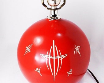 Könnte beinhalten: Eine rote Keramik-Tischlampe mit einem weißen Pinstripe-Design. Die Lampe hat einen runden Sockel und eine silberne Fassung.