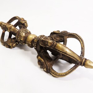 May include: A brass vajra, a ritual weapon in Buddhism, with intricate details and a pointed tip. The vajra symbolizes strength, power, and enlightenment.
