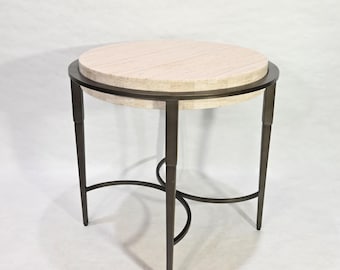 May include: A round side table with a light beige travertine top and a dark metal base. The base has four legs and a curved metal frame.