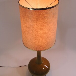 Może przedstawiać: Lampa stojąca w stylu mid-century modern z abażurem z białego materiału z złotą obwódką i zieloną ceramiczną podstawą.