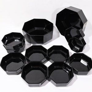 May include: A set of ten black octagonal bowls of varying sizes. The bowls are arranged in a circular pattern, with the largest bowl in the center and the smallest bowls on the outside.