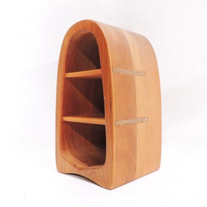 Pu&ograve; includere: Un'unit&agrave; a scaffale in legno con un design curvo e arrotondato. Lo scaffale ha tre ripiani ed &egrave; realizzato in legno marrone chiaro.
