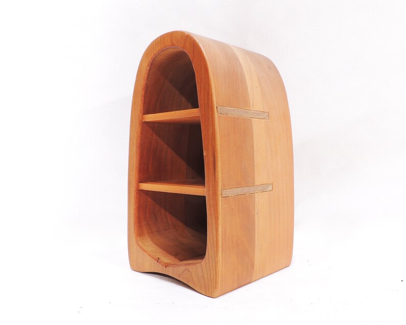 Pu&ograve; includere: Un'unit&agrave; a scaffale in legno con un design curvo e arrotondato. Lo scaffale ha tre ripiani ed &egrave; realizzato in legno marrone chiaro.