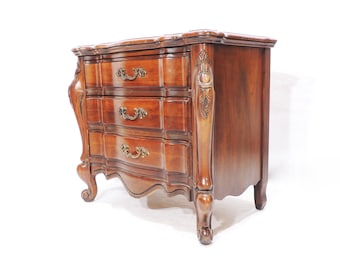 May include: A three-drawer wooden nightstand with ornate carvings and brass hardware. The nightstand has a rich brown finish and a curved front.
