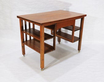 May include: A dark brown wooden desk with a shelf on the left side and a shelf on the right side. The desk has a drawer in the front and is on wheels.