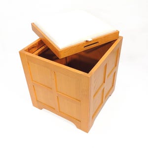 Peut inclure: Un coffre de rangement en bois brun clair avec un couvercle à charnière. Le couvercle est partiellement ouvert, révélant l'intérieur. Le coffre a une forme rectangulaire avec des côtés à panneaux.