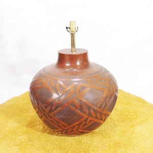 Puede incluir: Una lámpara de mesa de cerámica marrón con un patrón geométrico tallado en la superficie. La lámpara tiene una base de latón y una pantalla simple.