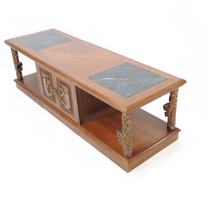 May include: A long, rectangular coffee table with a dark wood finish and carved legs. The table has two doors with carved details and a green marble top.
