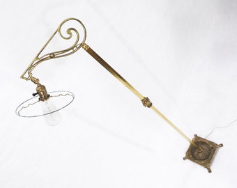 May include: A brass floor lamp with a decorative, scrolled arm and a clear glass shade. The lamp has a square base with an ornate design.