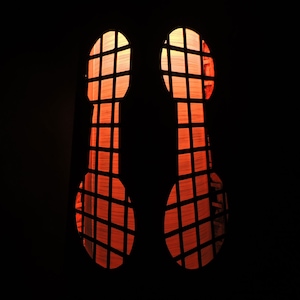 Puede incluir: Dos ventanas brillantes de color naranja rojizo con un patrón de rejilla, vistas desde el interior de una habitación oscura.