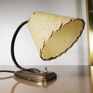 May include: A vintage desk lamp with a brown metal base and a beige fabric shade with a stitched edge. The lamp has a single switch on the base.