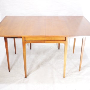 May include: A light wood drop leaf table with a single drawer. The table has four legs and is made of solid wood.
