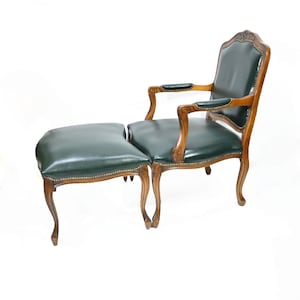 Op de afbeelding: Een antieke fauteuil en bijpassende ottoman set. De stoel heeft een donkergroene leren zitting en rugleuning, met houten armleuningen en frame. De ottoman is van bijpassend donkergroen leer. De set heeft een klassiek, elegant ontwerp.