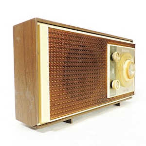 May include: A vintage brown and white AM/FM radio with a woodgrain finish and a speaker grille. The radio has a large tuning knob and a smaller volume knob. The radio is labeled "Majestic" on the front.