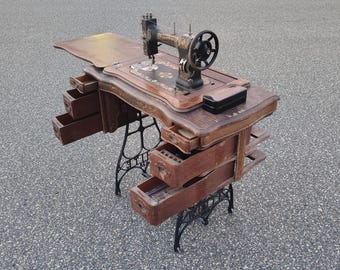 Máquina de coser antigua blanca rotativa de pedal alojada en un mueble de madera original. Mesa rústica.