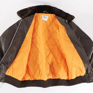 May include: A brown bomber jacket with a faux fur collar and an orange quilted lining. The jacket has a zipper closure and a ribbed hem. The jacket is open, displaying the bright orange interior.