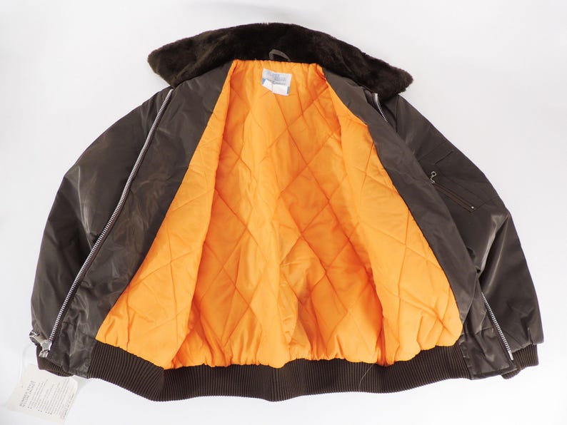 May include: A brown bomber jacket with a faux fur collar and an orange quilted lining. The jacket has a zipper closure and a ribbed hem. The jacket is open, displaying the bright orange interior.