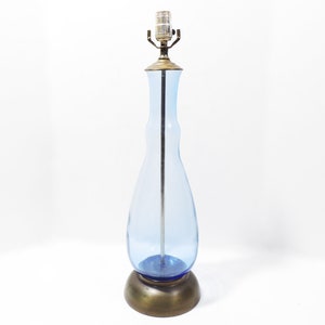 May include: A blue glass table lamp with a brass base and a clear glass shade. The lamp has a simple, elegant design.