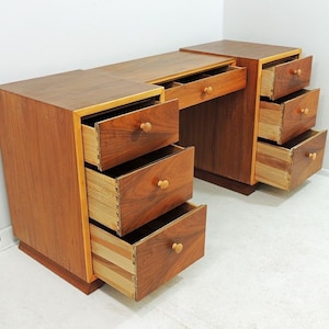 May include: A vintage wooden desk with a light brown finish and multiple drawers. The desk has a simple design with a rectangular top and a series of drawers on either side.