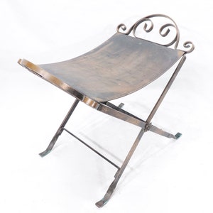 May include: A rustic, antique-style, metal folding stool with a curved, ornate top and a distressed bronze finish.