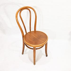 May include: A wooden chair with a curved back and a round seat. The chair is made of light brown wood and has a natural finish.
