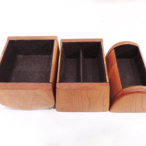 Pu&ograve; includere: Tre scatole di legno con rivestimento in feltro marrone. Le scatole sono di dimensioni e forme diverse. La scatola a sinistra &egrave; quadrata, la scatola al centro &egrave; rettangolare e la scatola a destra &egrave; curva.