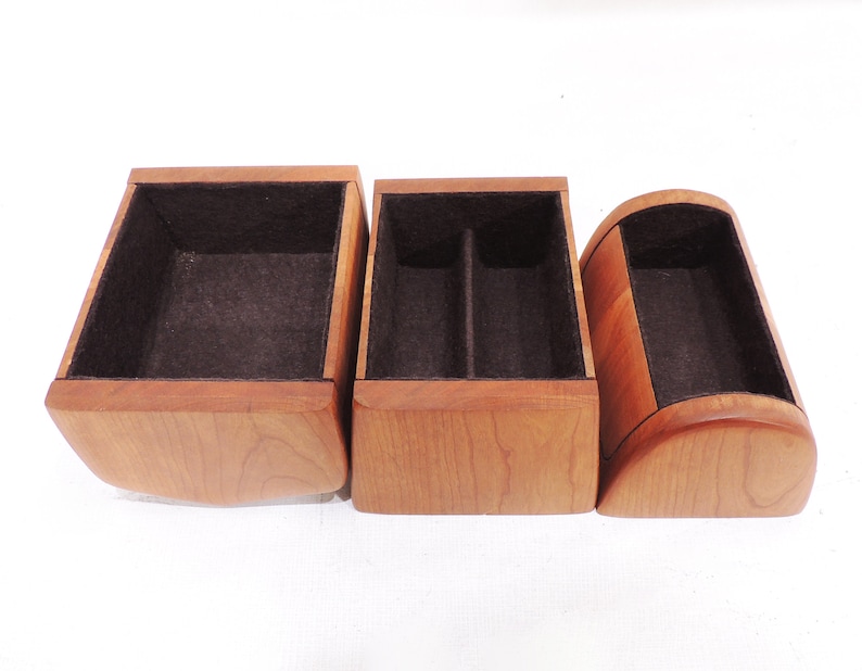 Pu&ograve; includere: Tre scatole di legno con rivestimento in feltro marrone. Le scatole sono di dimensioni e forme diverse. La scatola a sinistra &egrave; quadrata, la scatola al centro &egrave; rettangolare e la scatola a destra &egrave; curva.